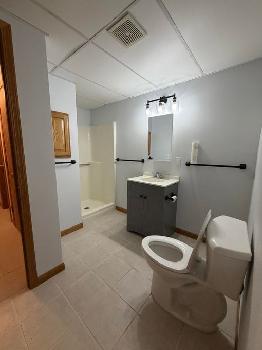 Small bathroom with toilet, vanity sink, mirror, and tiled floor in white and gray.