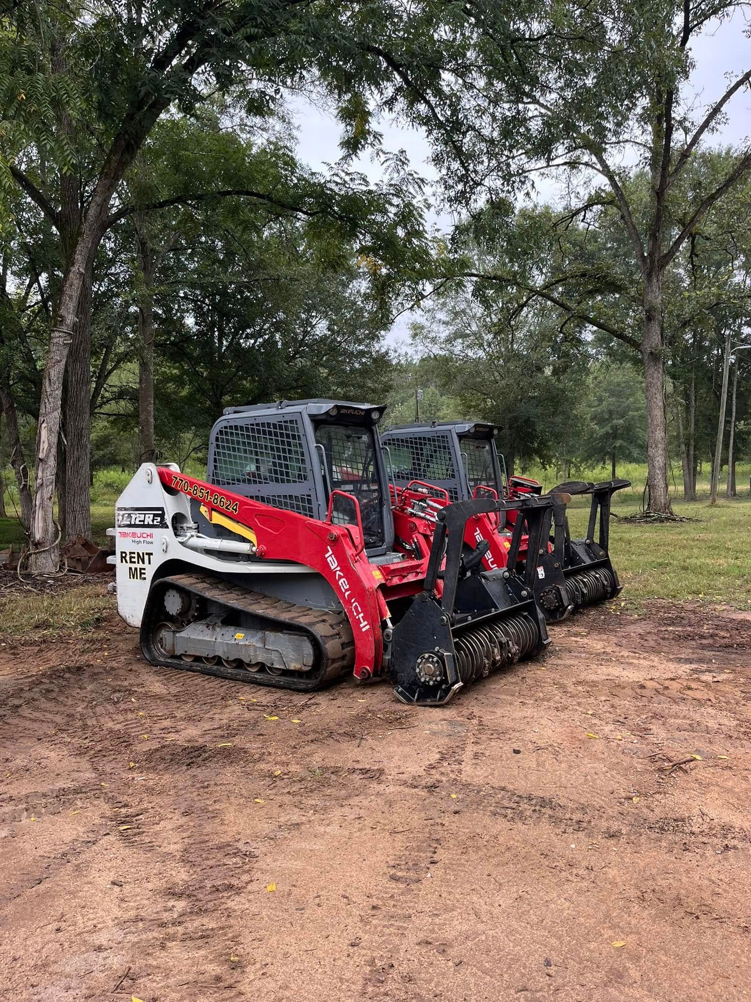 Red skid-steer loader with brush cutter attachment on a dirt path in a wooded area