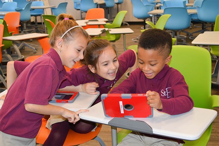 A boy and two girls are looking at a tablet in a classroom.