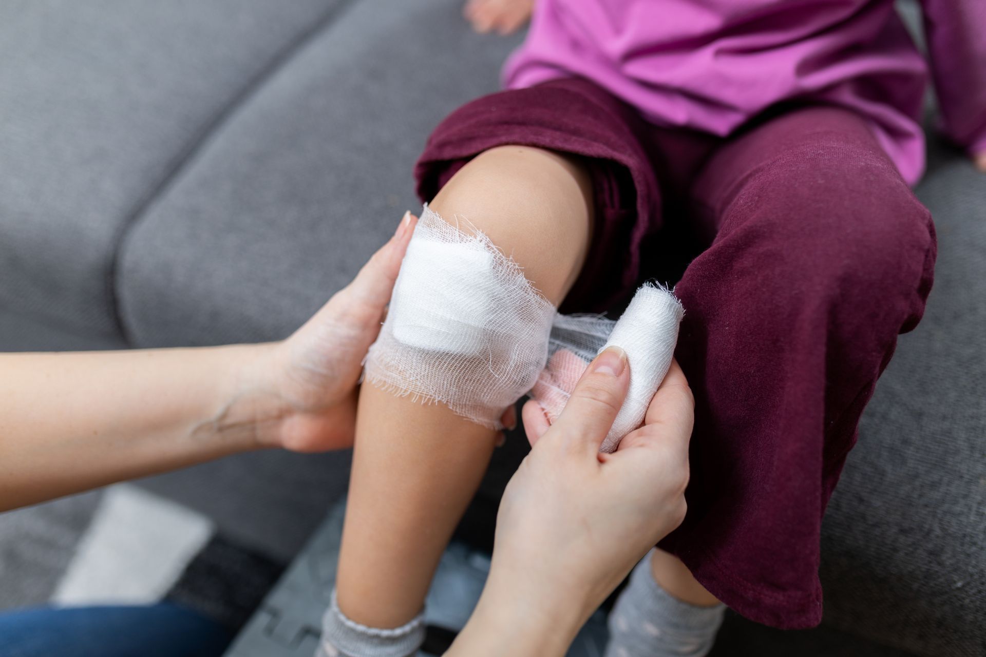 An adult gently wraps a bandage around a child’s knee to cover a small injury.