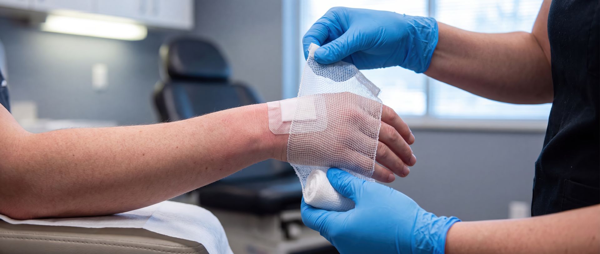 Medical professional in blue gloves wrapping a patient's injured wrist with a white gauze bandage
