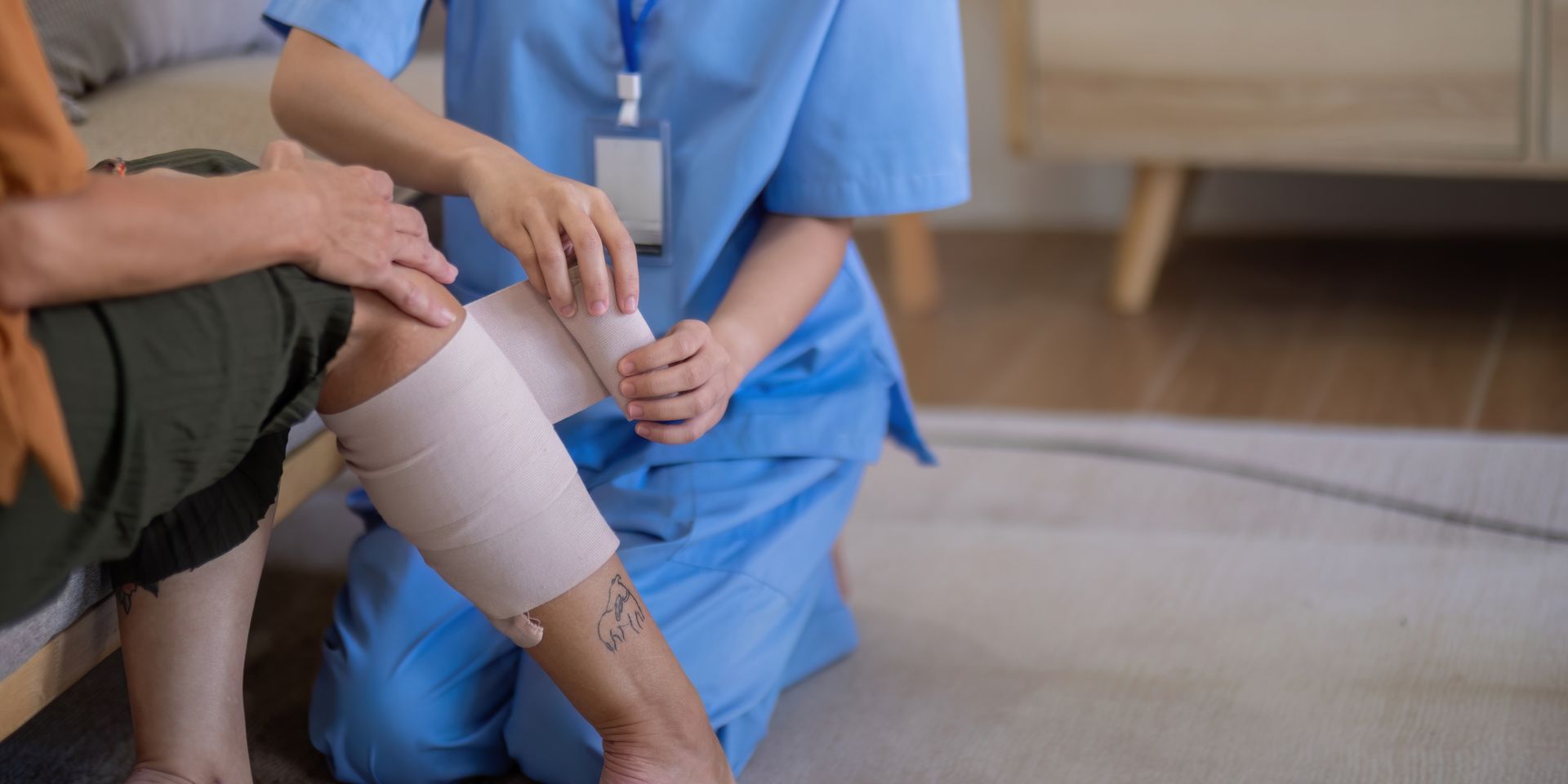 A healthcare provider in scrubs wraps a compression bandage around a patient's lower leg
