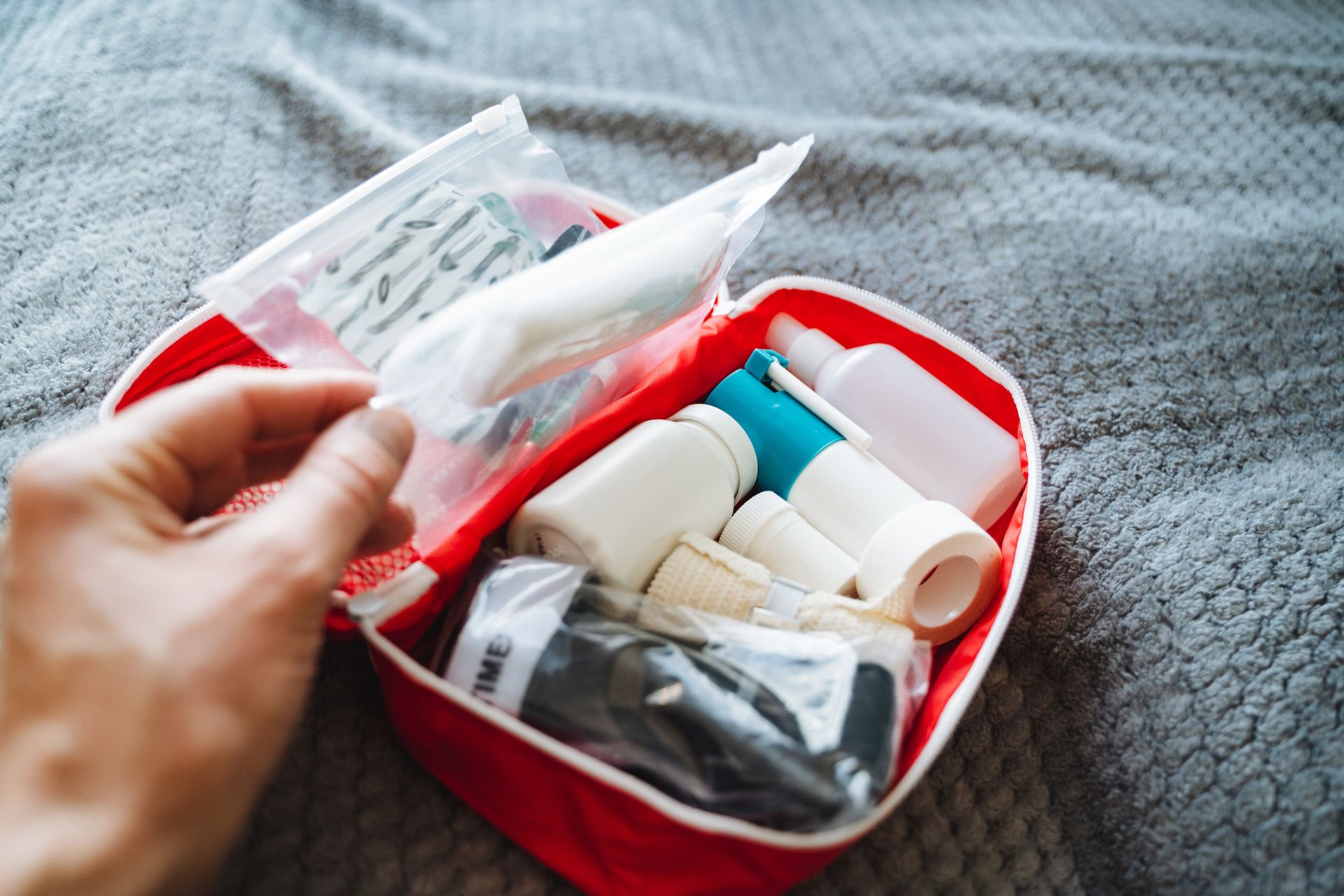 A person is slowly and carefully opening a first aid kit that is placed on a bed.