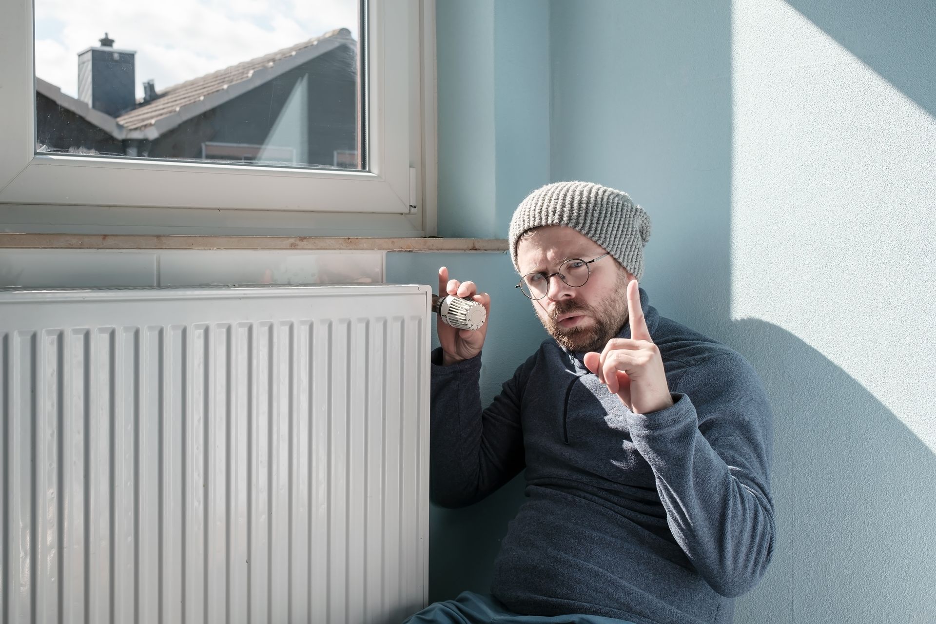 A man is sitting in front of a radiator holding a light bulb.