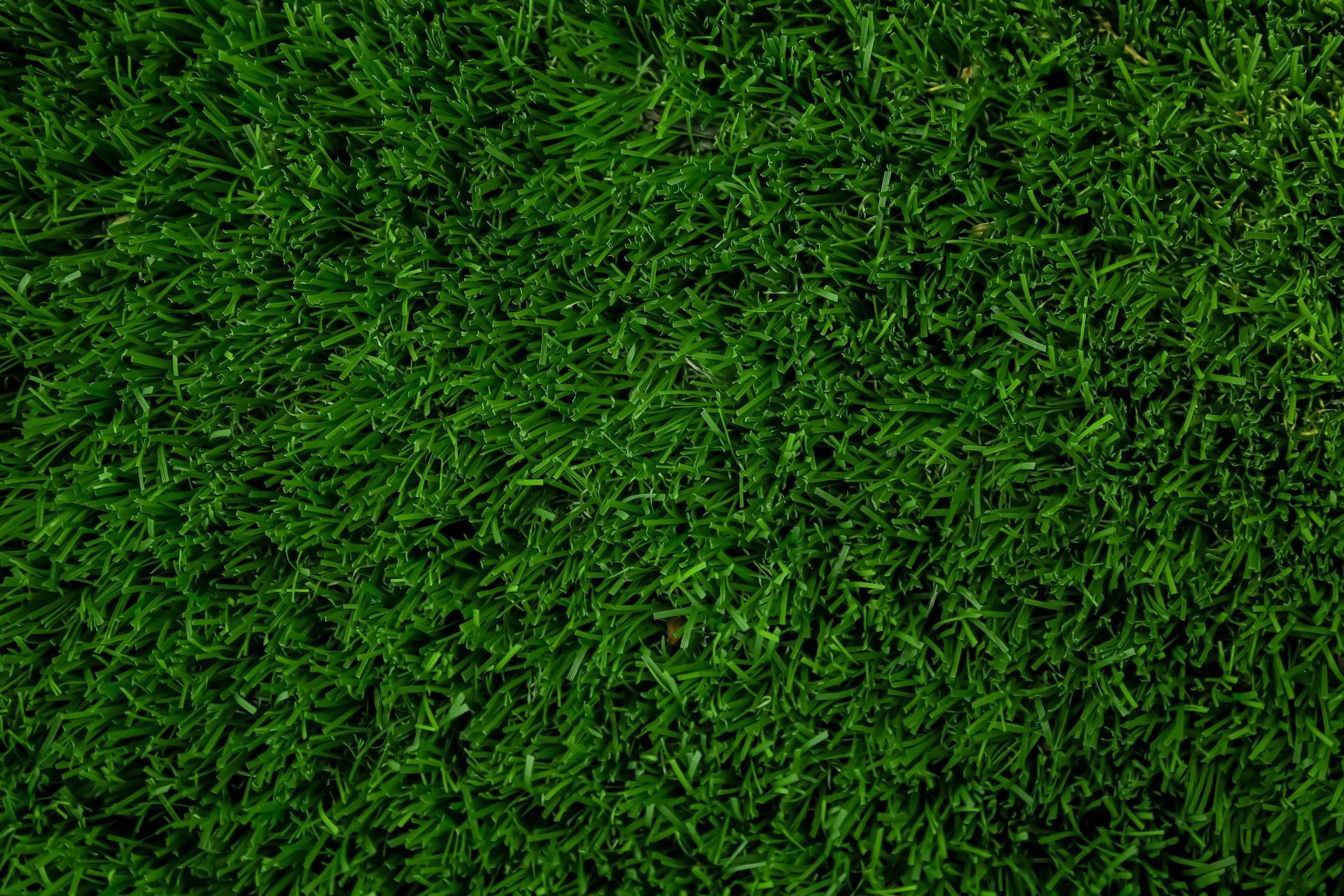 Gardener trimming hedges along a bright green lawn with a lawn mower nearby
