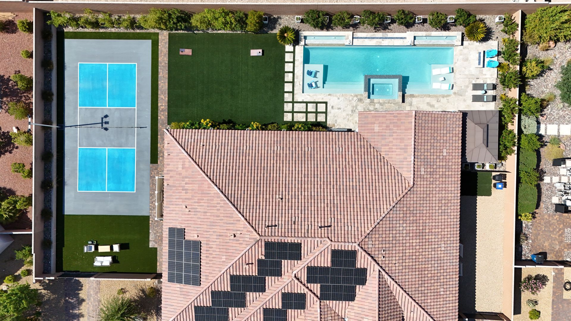 Aerial view of a residential property with a tiled roof, swimming pool, green lawn, and a blue pickleball court.