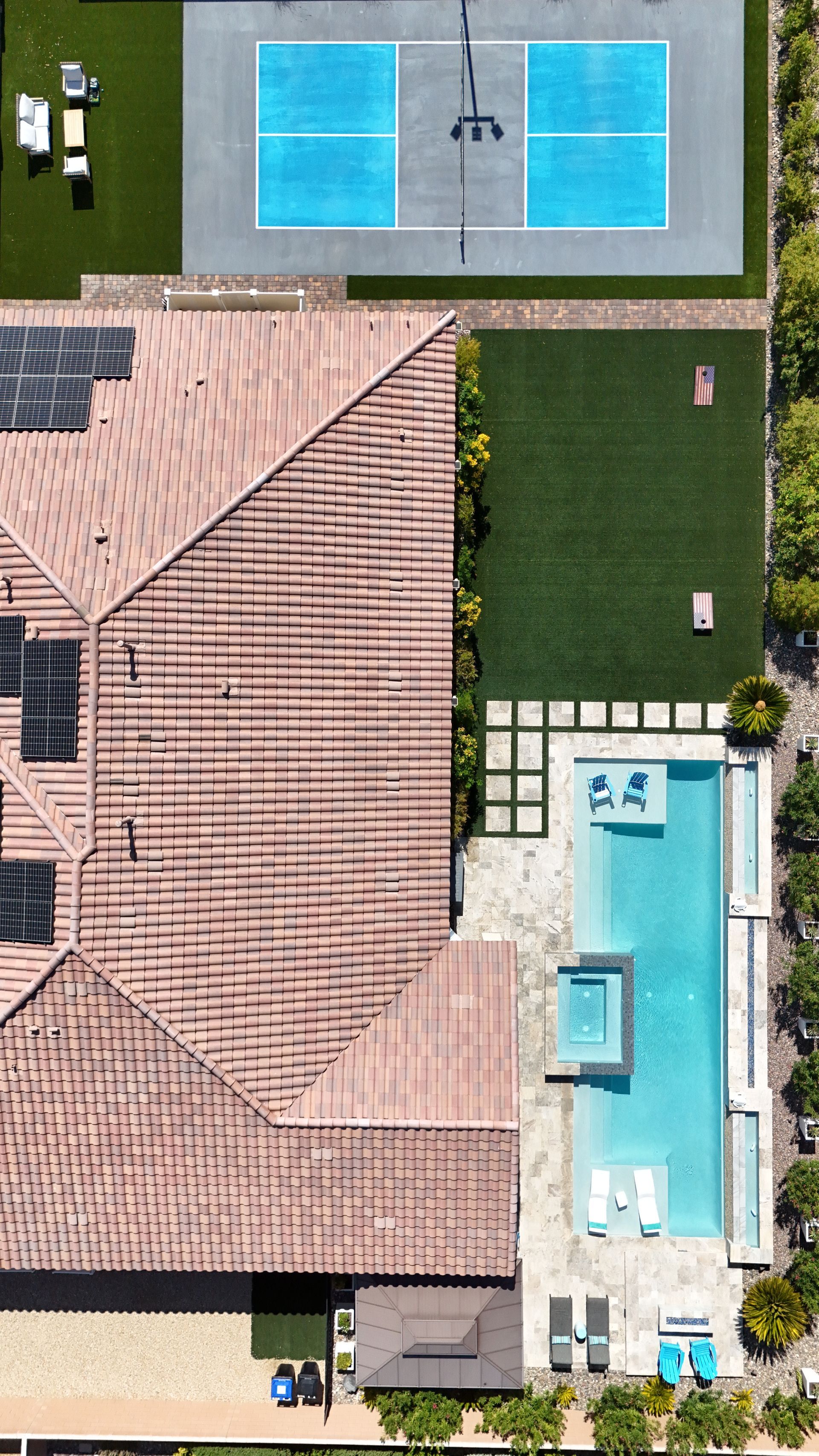 Aerial view of a home with a red-tiled roof, a pickleball court, a swimming pool with a spa, and green lawn space.