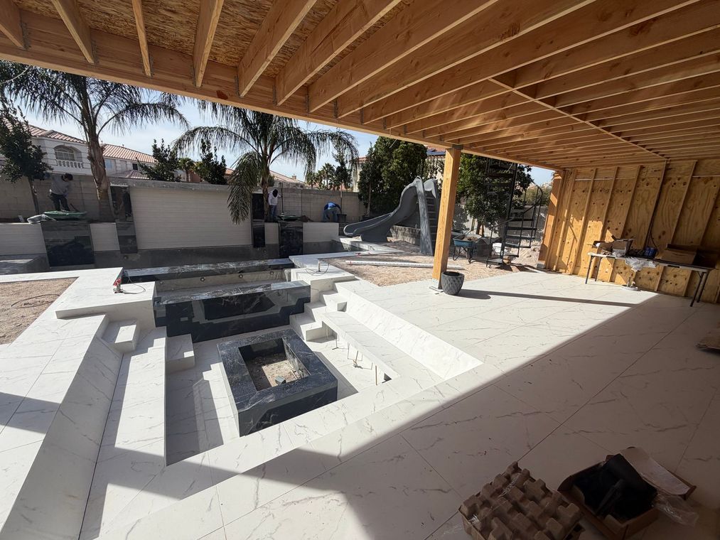 A partially shaded outdoor patio features a sunken seating area with black stone fire pits against a light tiled floor.