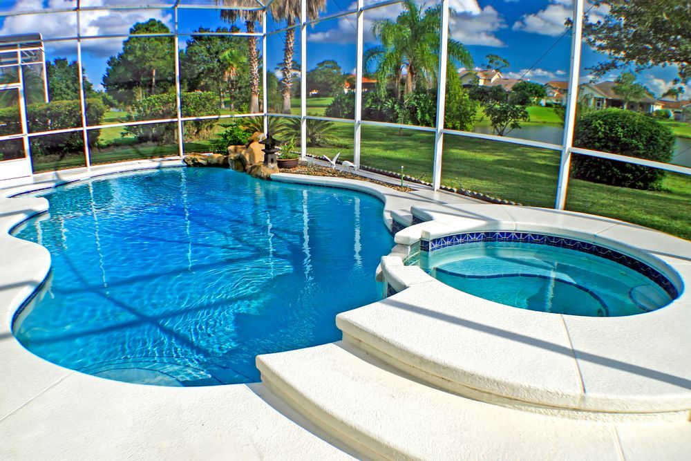 A screened-in patio featuring a bright blue swimming pool and a connected circular hot tub on a sunny day.
