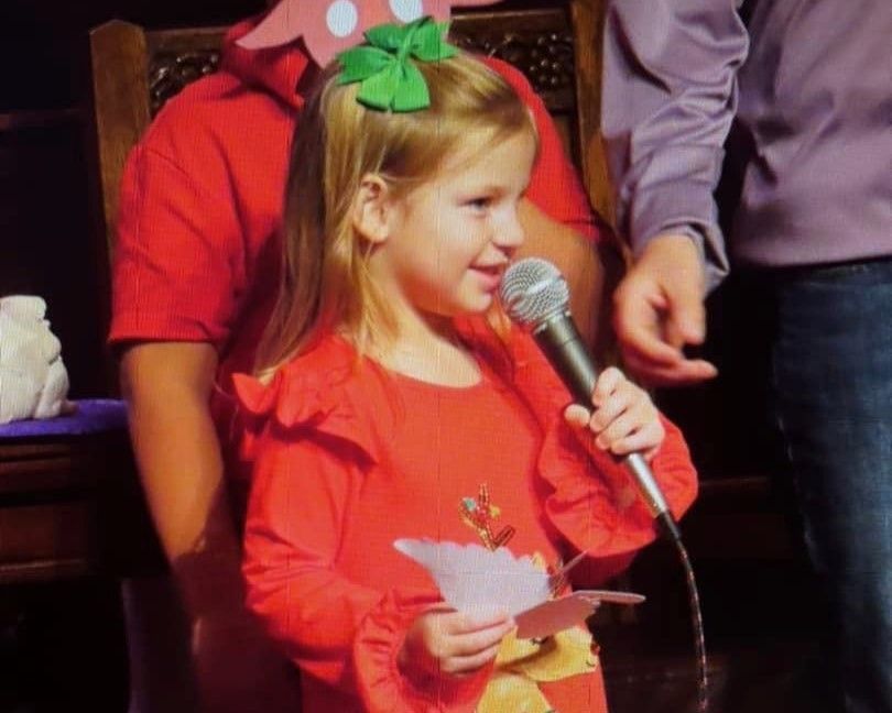 A little girl in a red jacket is holding a microphone
