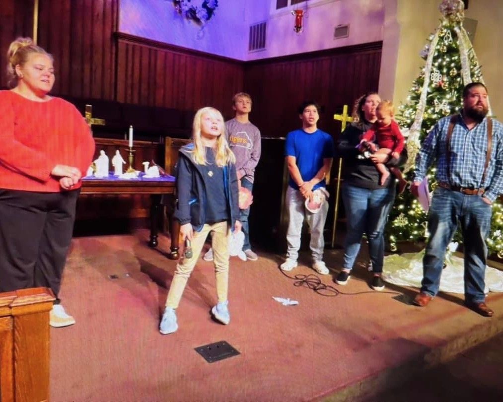 A group of people are standing in a church in front of a christmas tree.