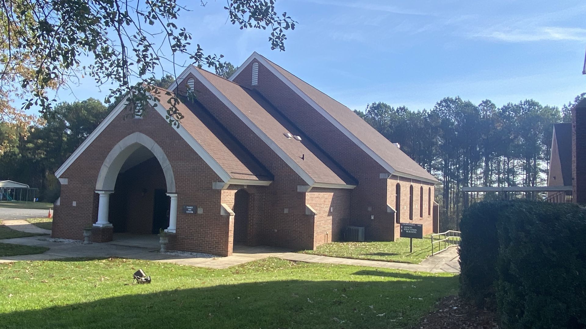 A brick building with a brown roof is surrounded by grass and trees