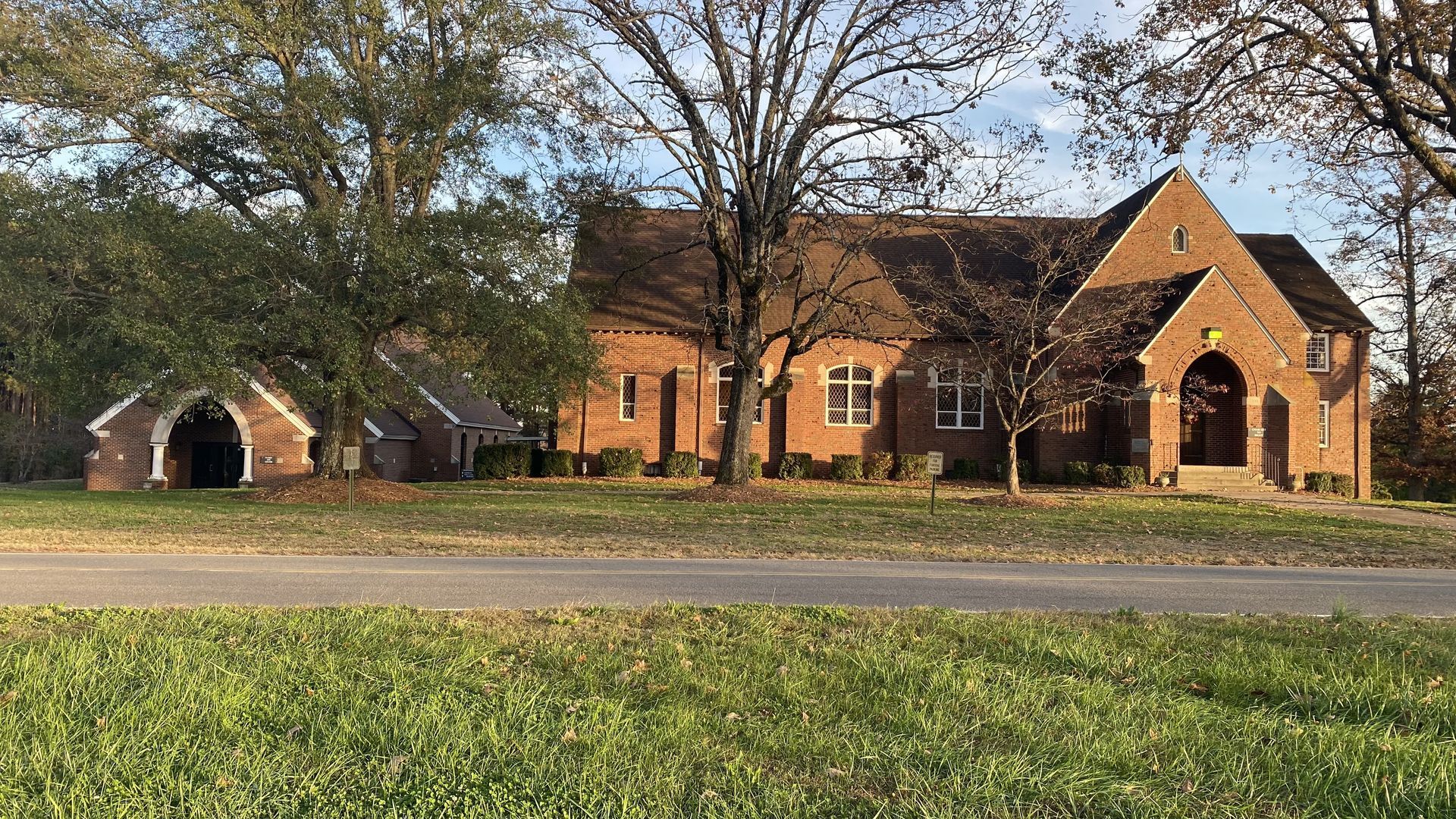 A large brick house is sitting on top of a lush green field next to a road.