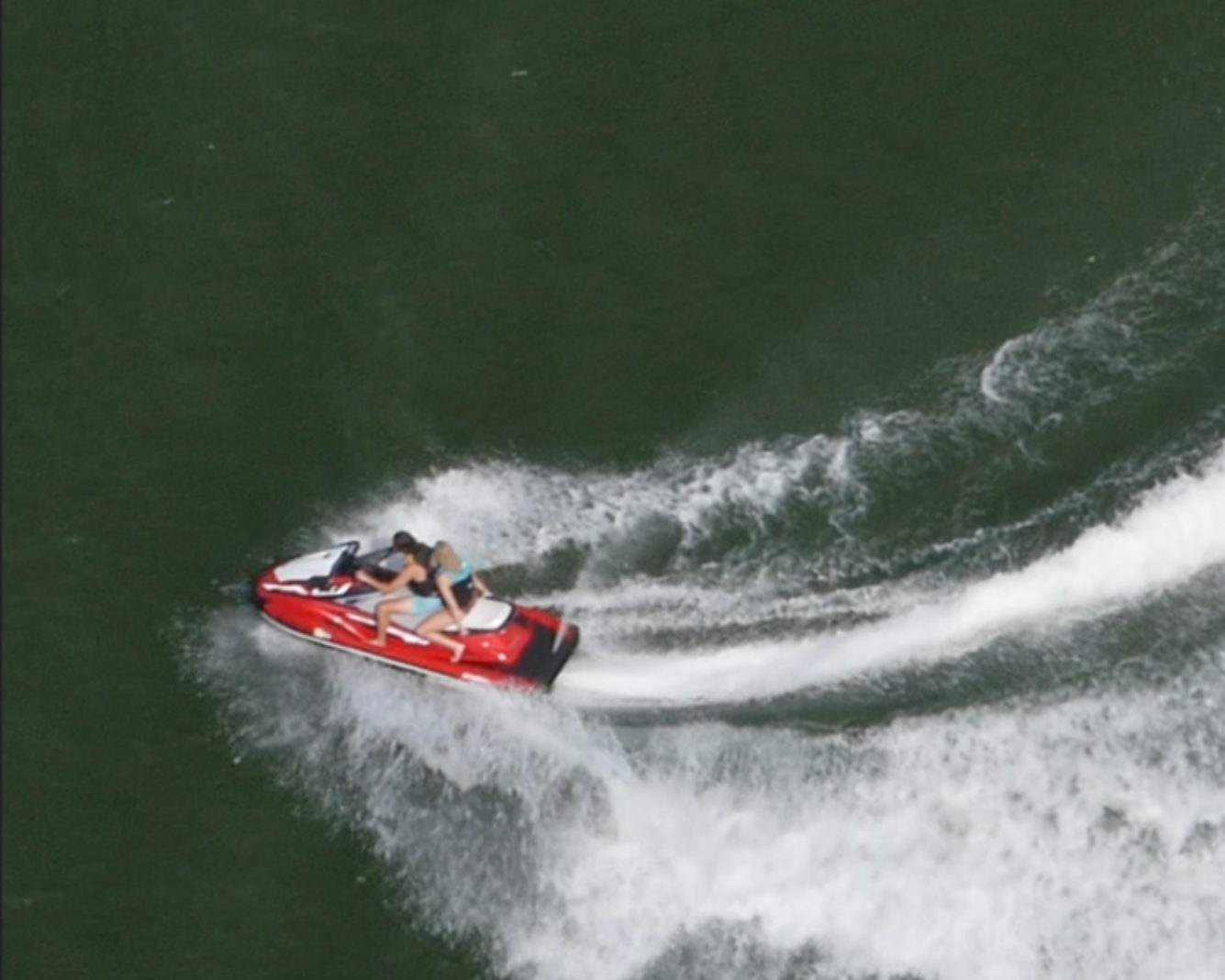 Red speedboat carving through dark green water, leaving a white foamy wake.
