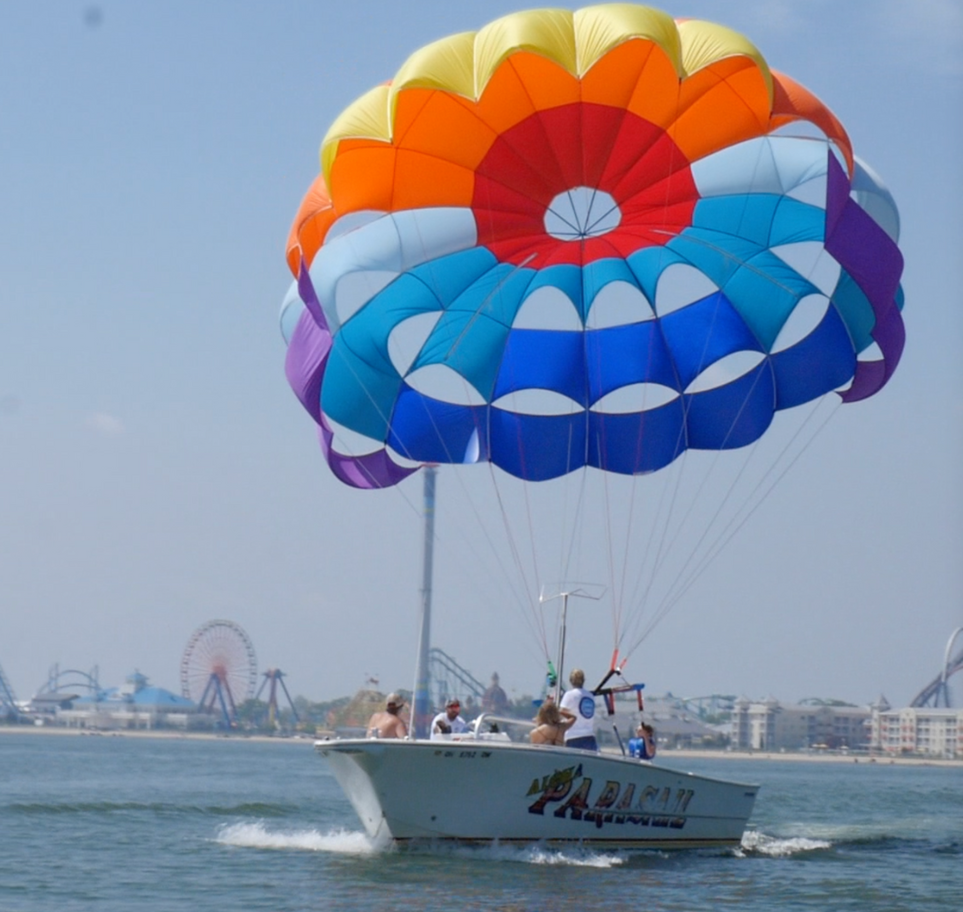 Parasailing boat on calm water with a colorful rainbow parachute overhead