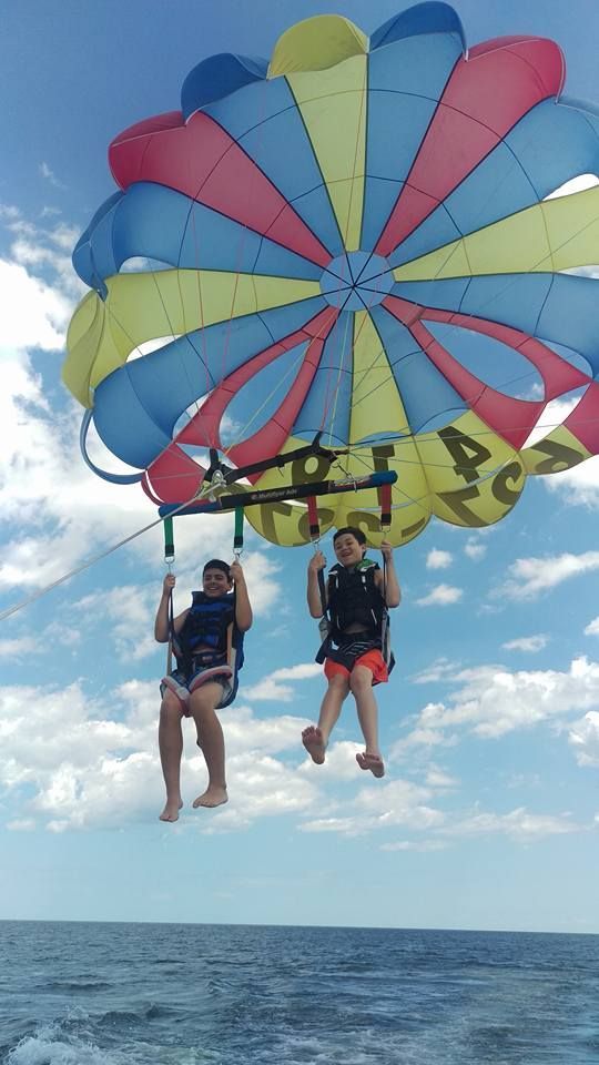 Two people parasailing above the ocean under a colorful parachute canopy
