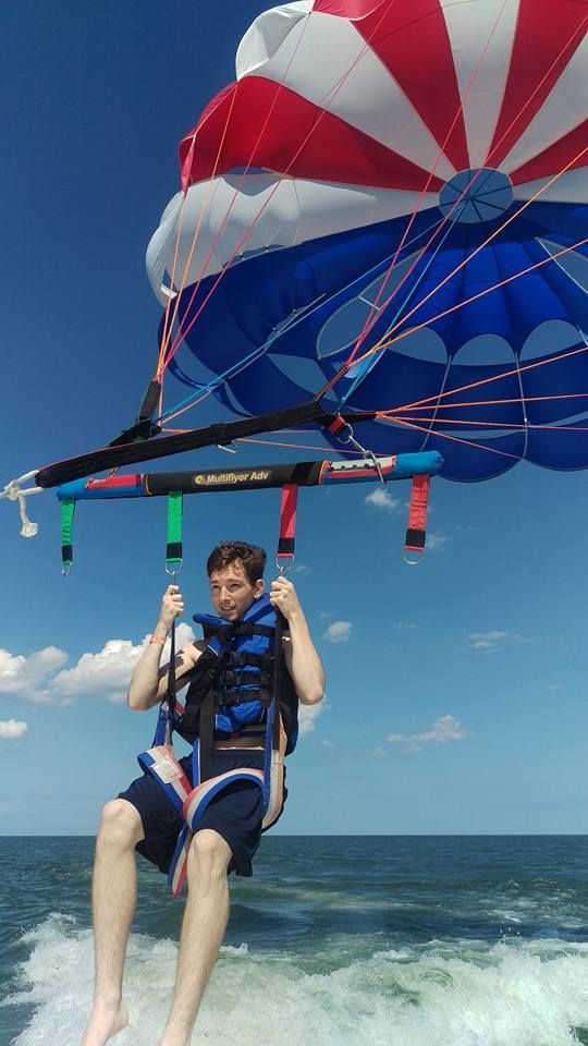 Person parasailing over the ocean beneath a red, white, and blue canopy, feet dangling above the water