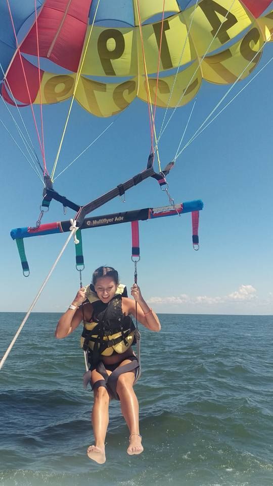 Person parasailing over the ocean under a colorful canopy, wearing a life vest and smiling.