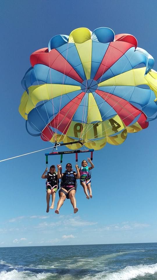 People parasailing over the ocean beneath a colorful striped canopy under a clear blue sky
