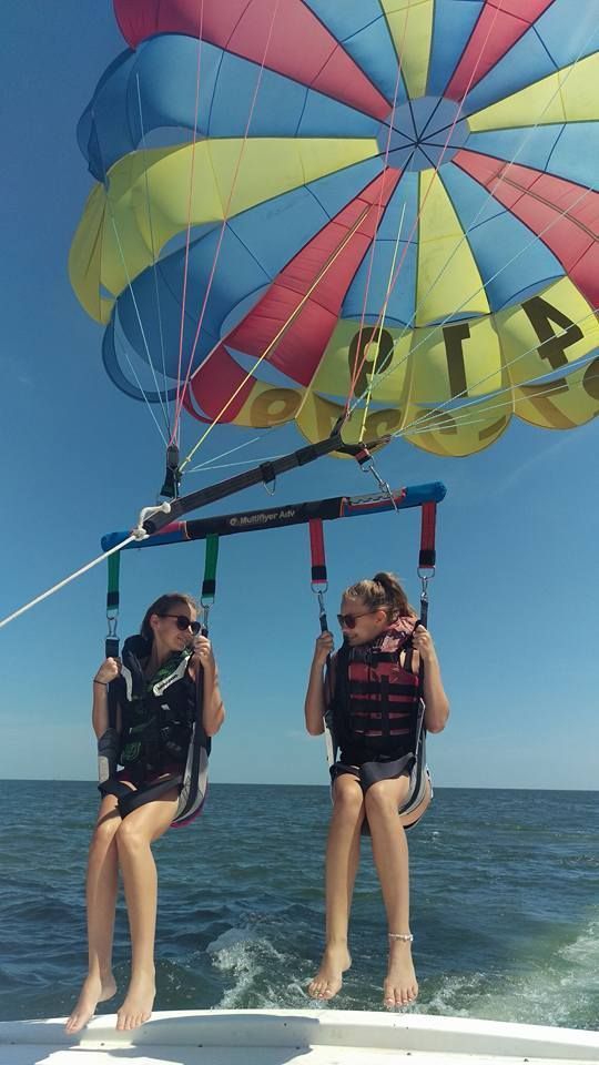 Two people parasailing over the ocean beneath a colorful canopy, feet dangling above the water