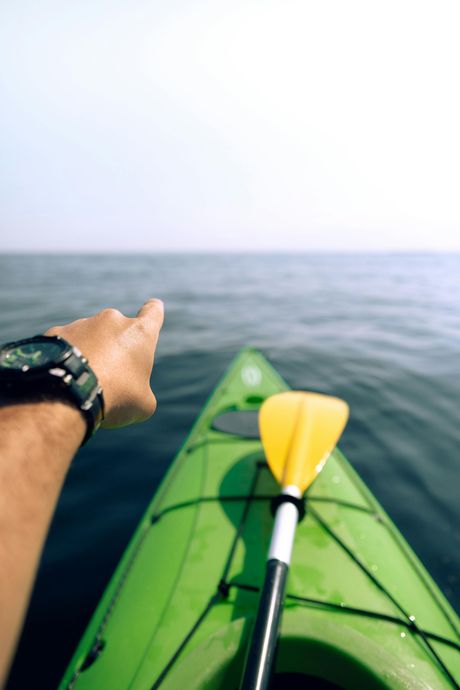 Kayaking on calm water, pointing toward the horizon from a green kayak with a yellow paddle.