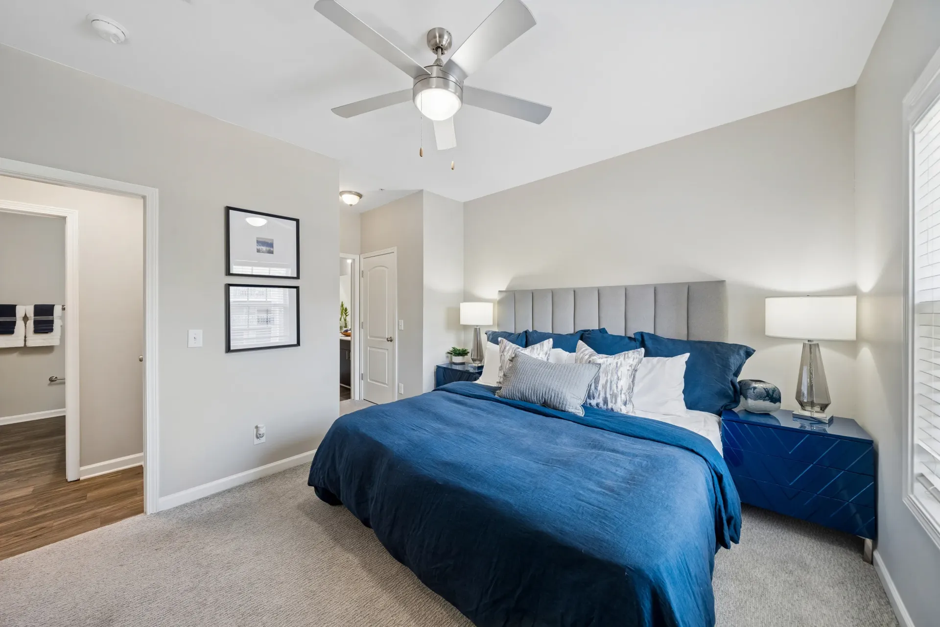 Bedroom with a king-size bed, blue bedding, a ceiling fan, and a doorway to a bathroom.