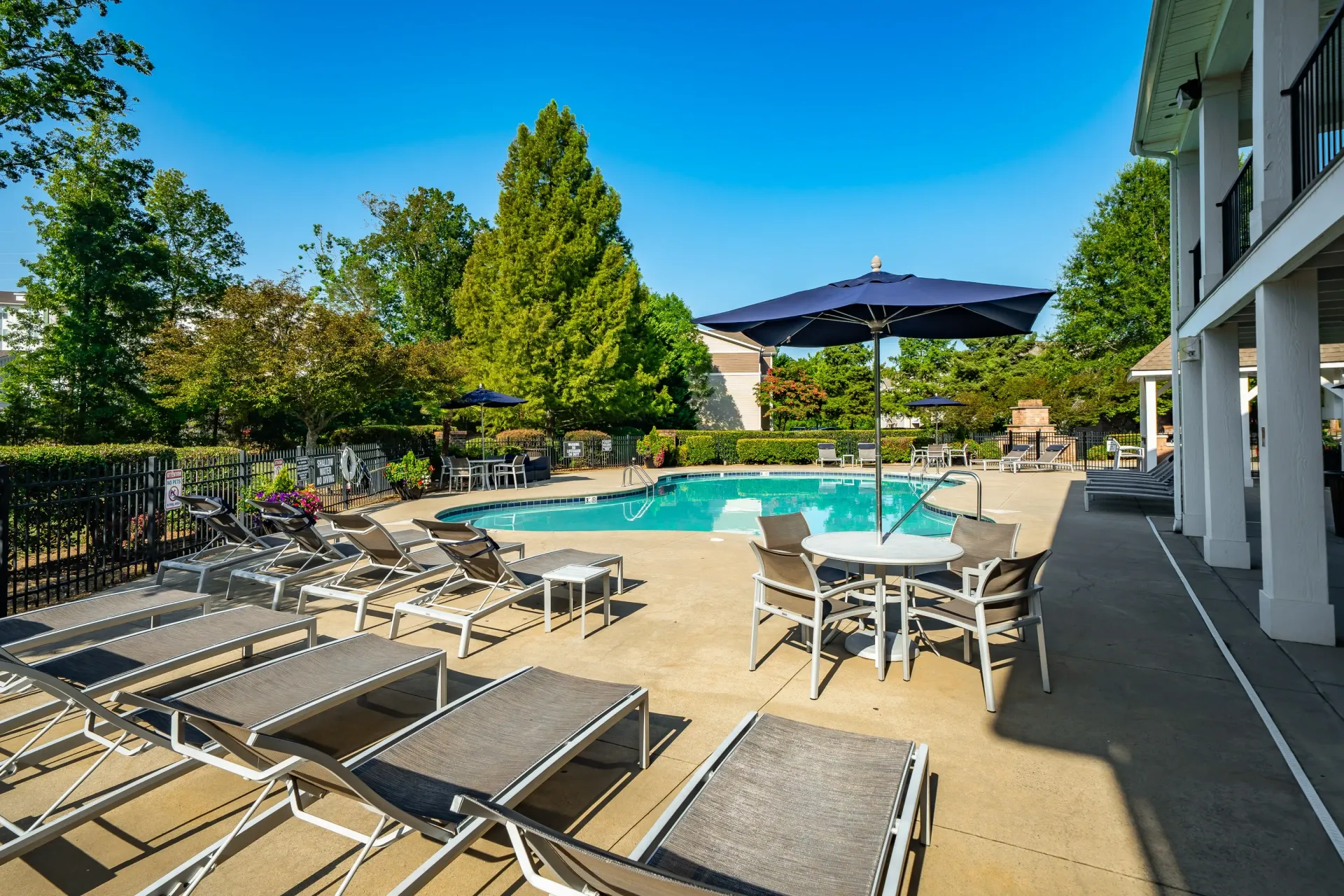 Outdoor swimming pool with lounge chairs and tables under umbrellas.