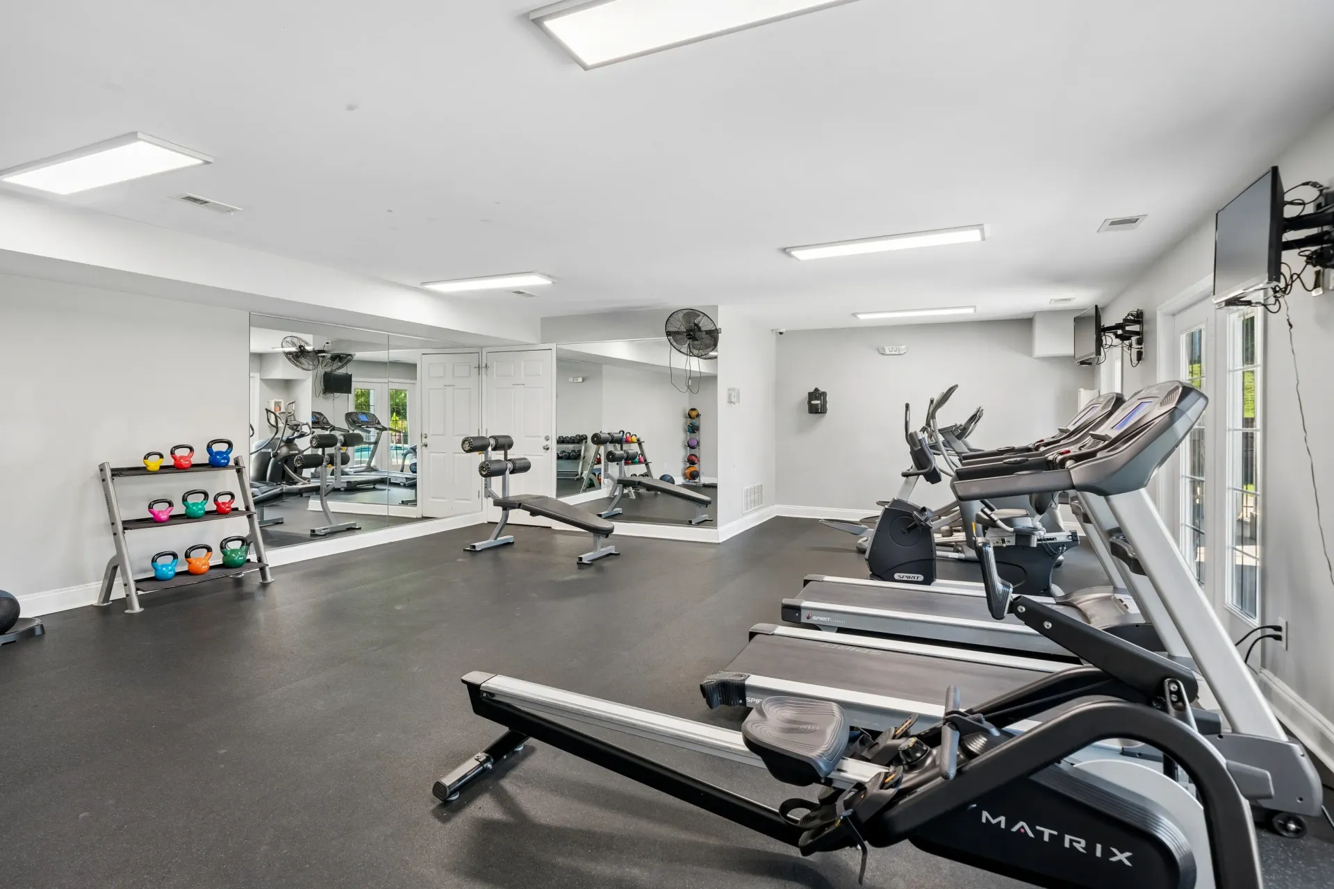 Fitness center with treadmills, elliptical machines, rowing machine, weight rack, and benches.