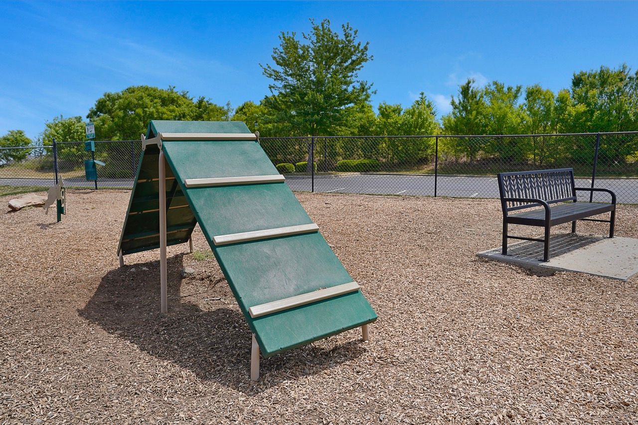 Playground with a green climbing ramp, bench, and chain-link fence in a gravel area at Reserve at Stone Hollow in Charlotte, NC.