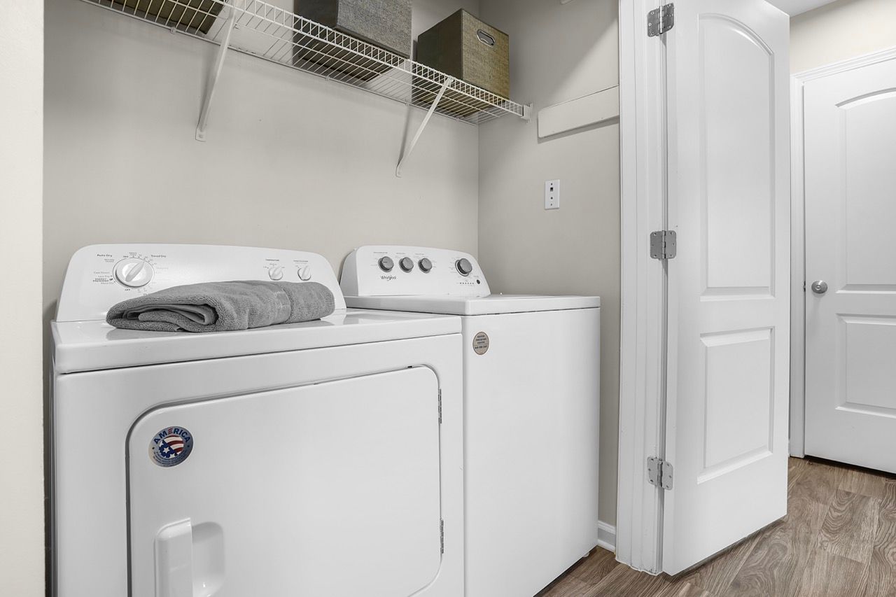 White washer and dryer in a compact laundry closet with a wire shelf and storage bins at Reserve at Stone Hollow in Charlotte, NC.