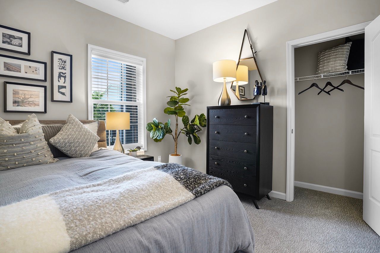 Bedroom in an apartment with a bed, dresser, plant, and open closet at Reserve at Stone Hollow in Charlotte, NC.