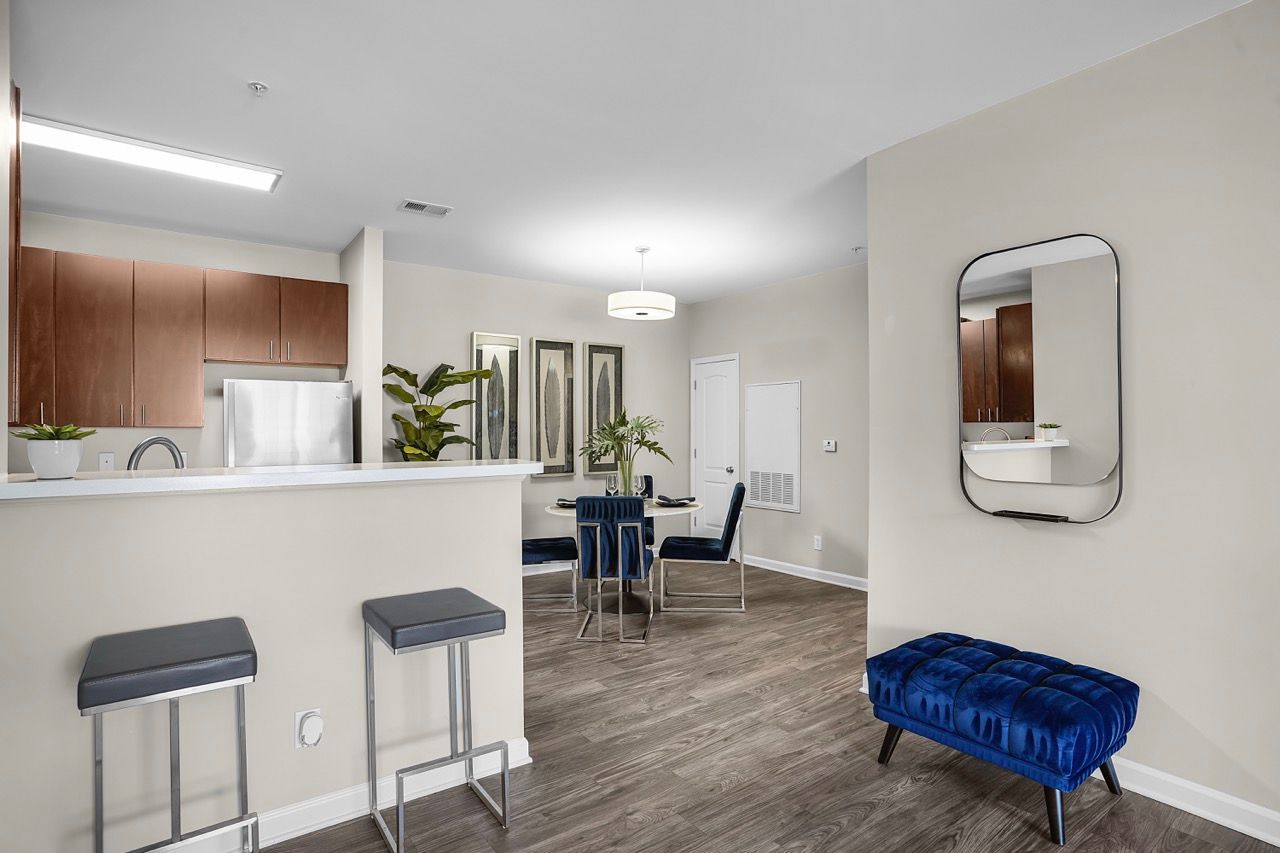Open-concept kitchen and dining area in a modern apartment with a bar counter, stools, and a blue tufted bench at Reserve at Stone Hollow in Charlotte, NC.
