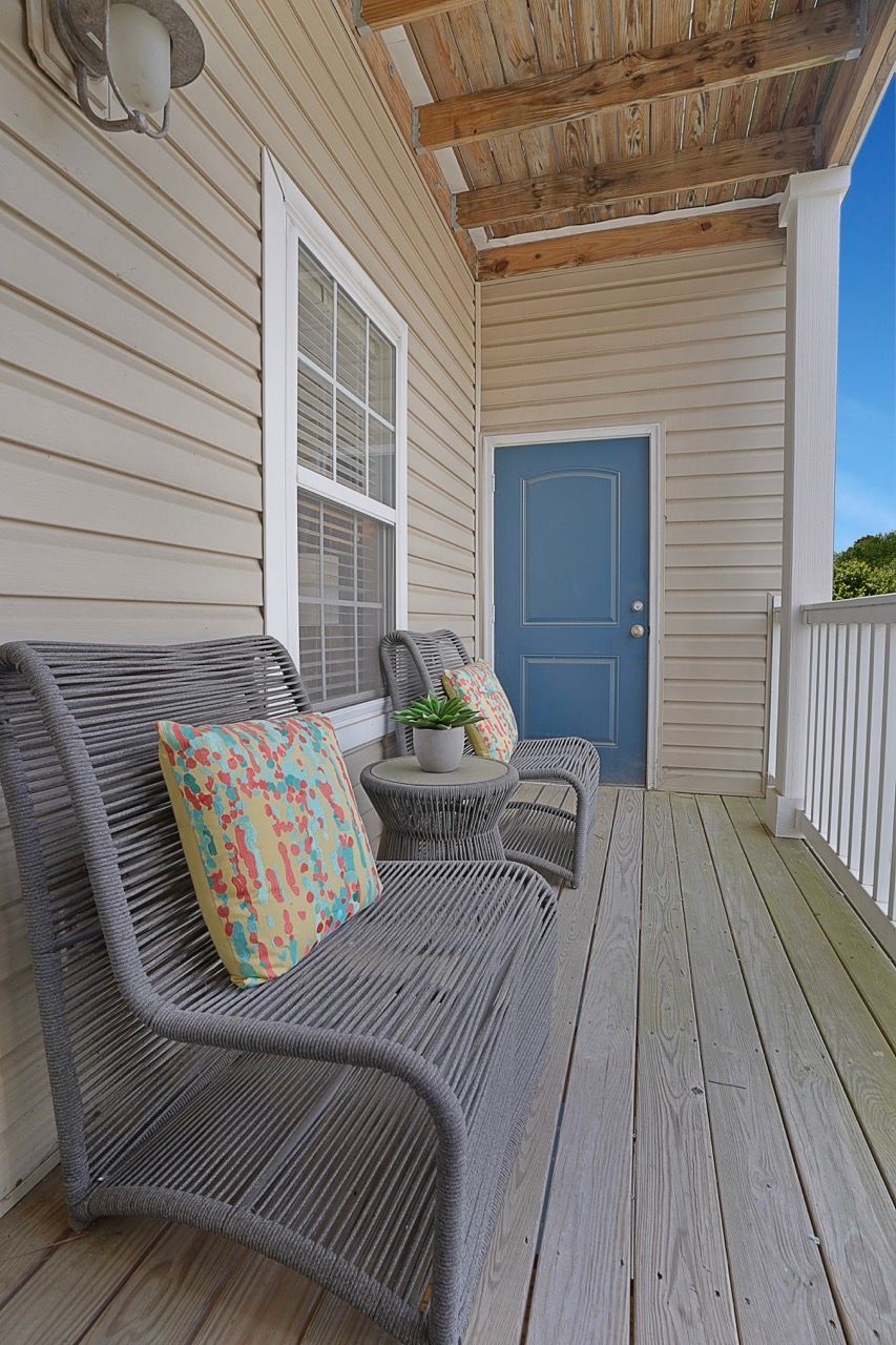 Front porch balcony with beige siding, blue door, two wicker chairs, and a small table at Reserve at Stone Hollow in Charlotte, NC.