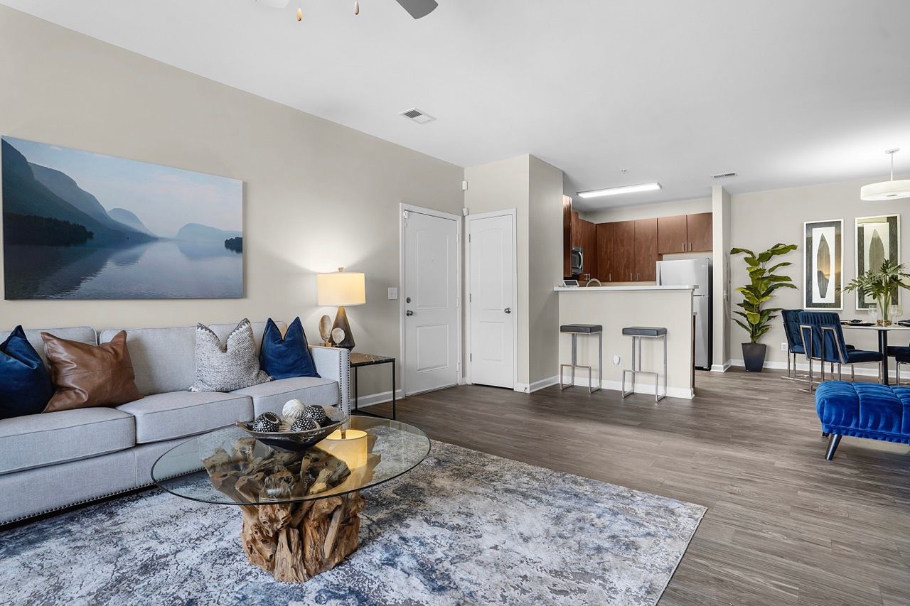 Open-concept living area with gray sofa, glass coffee table, and kitchen in the background at Reserve at Stone Hollow in Charlotte, NC.