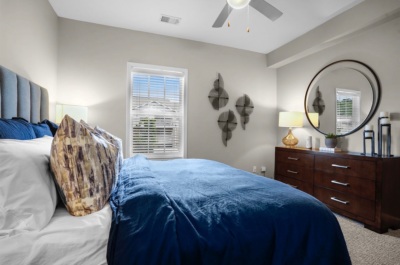 Bedroom in an apartment with blue bedding, a dark wood dresser, and a round mirror at Reserve at Stone Hollow in Charlotte, NC.