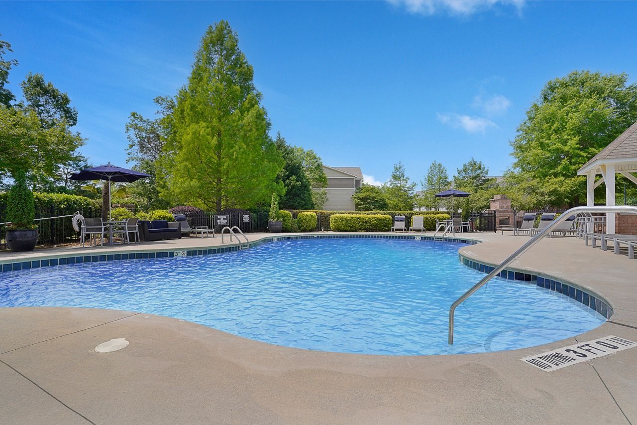 Pool area with blue water, surrounded by trees, loungers, and a gazebo under a blue sky at Reserve at Stone Hollow in Charlotte, NC.