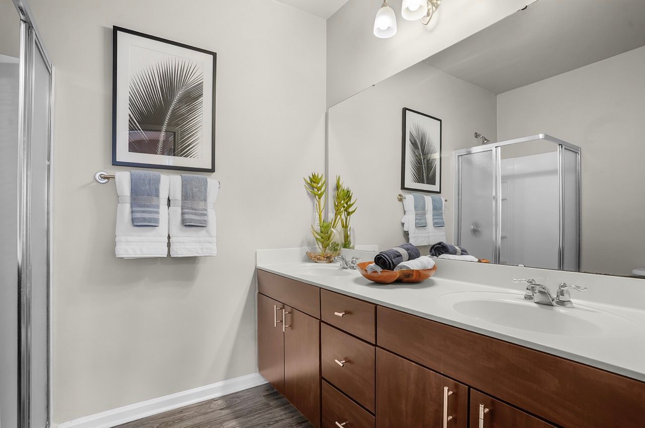 Bathroom with double vanity, wood cabinets, large mirror, framed art, towels, and glass shower at Reserve at Stone Hollow in Charlotte, NC.
