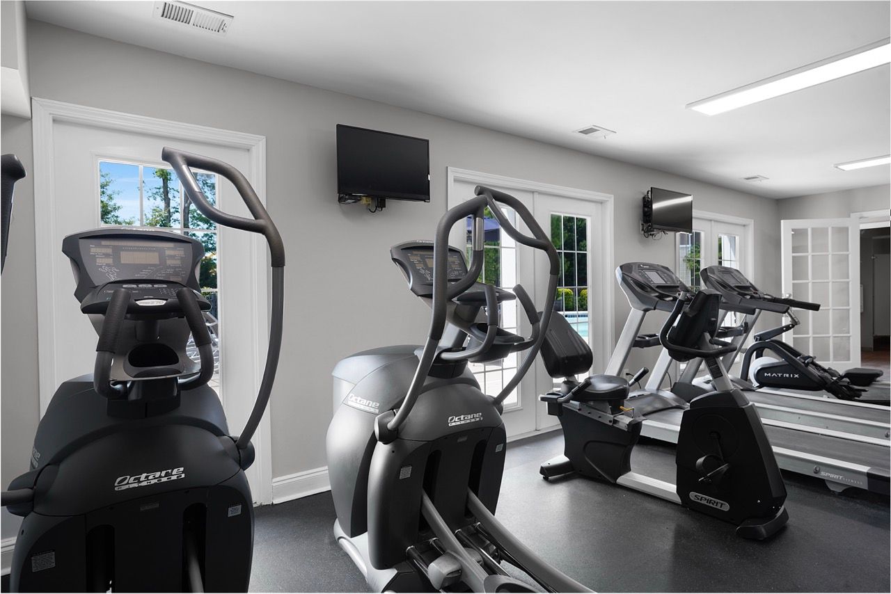 Interior view of a community fitness center with treadmills and ellipticals by windows at Reserve at Stone Hollow in Charlotte, NC.