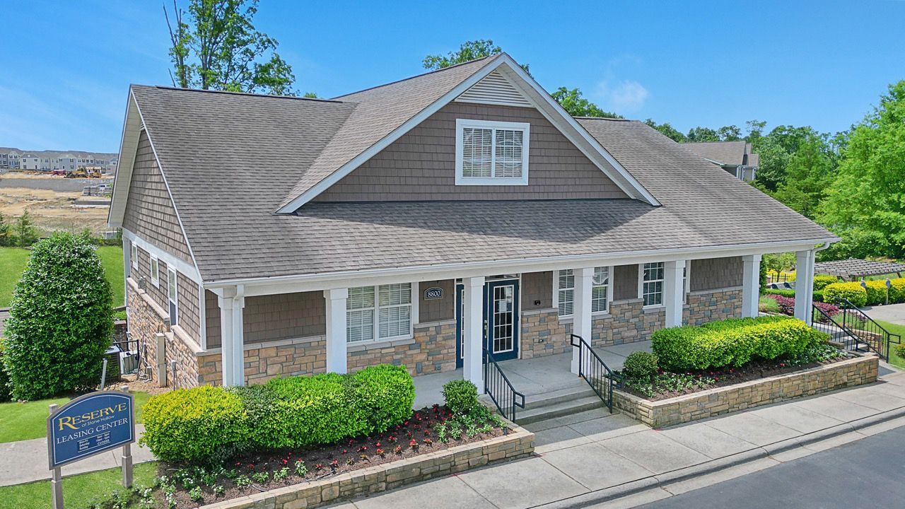 Exterior view of a leasing center building with stone accents and landscaped front planters at Reserve at Stone Hollow in Charlotte, NC.