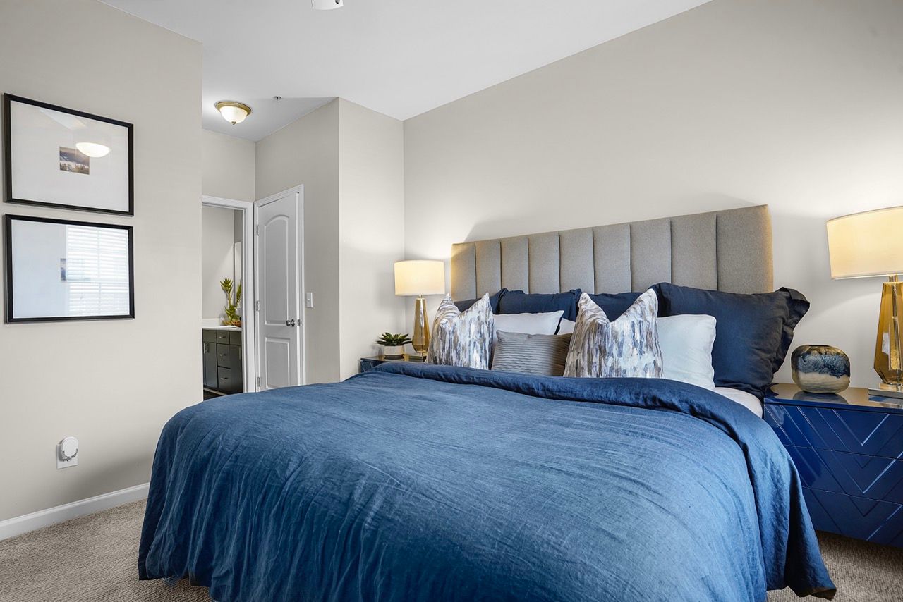 Bedroom with a large bed, blue duvet, upholstered headboard, and two matching nightstands with lamps at Reserve at Stone Hollow in Charlotte, NC.