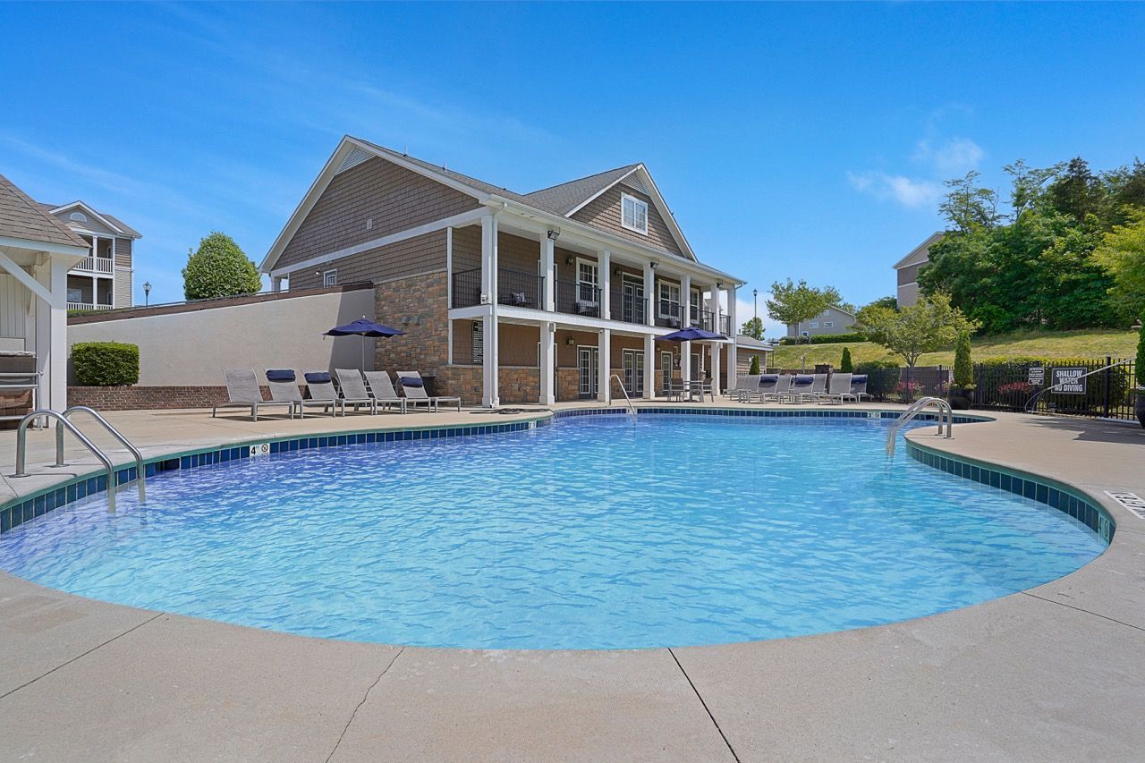 Outdoor apartment community pool with lounge chairs and a two-story clubhouse under a clear blue sky at Reserve at Stone Hollow in Charlotte, NC.