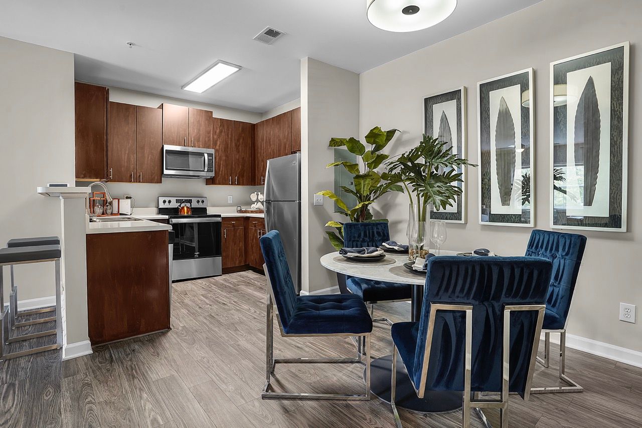 Open kitchen and dining area with dark wood cabinets, stainless appliances, and blue upholstered chairs at Reserve at Stone Hollow in Charlotte, NC.