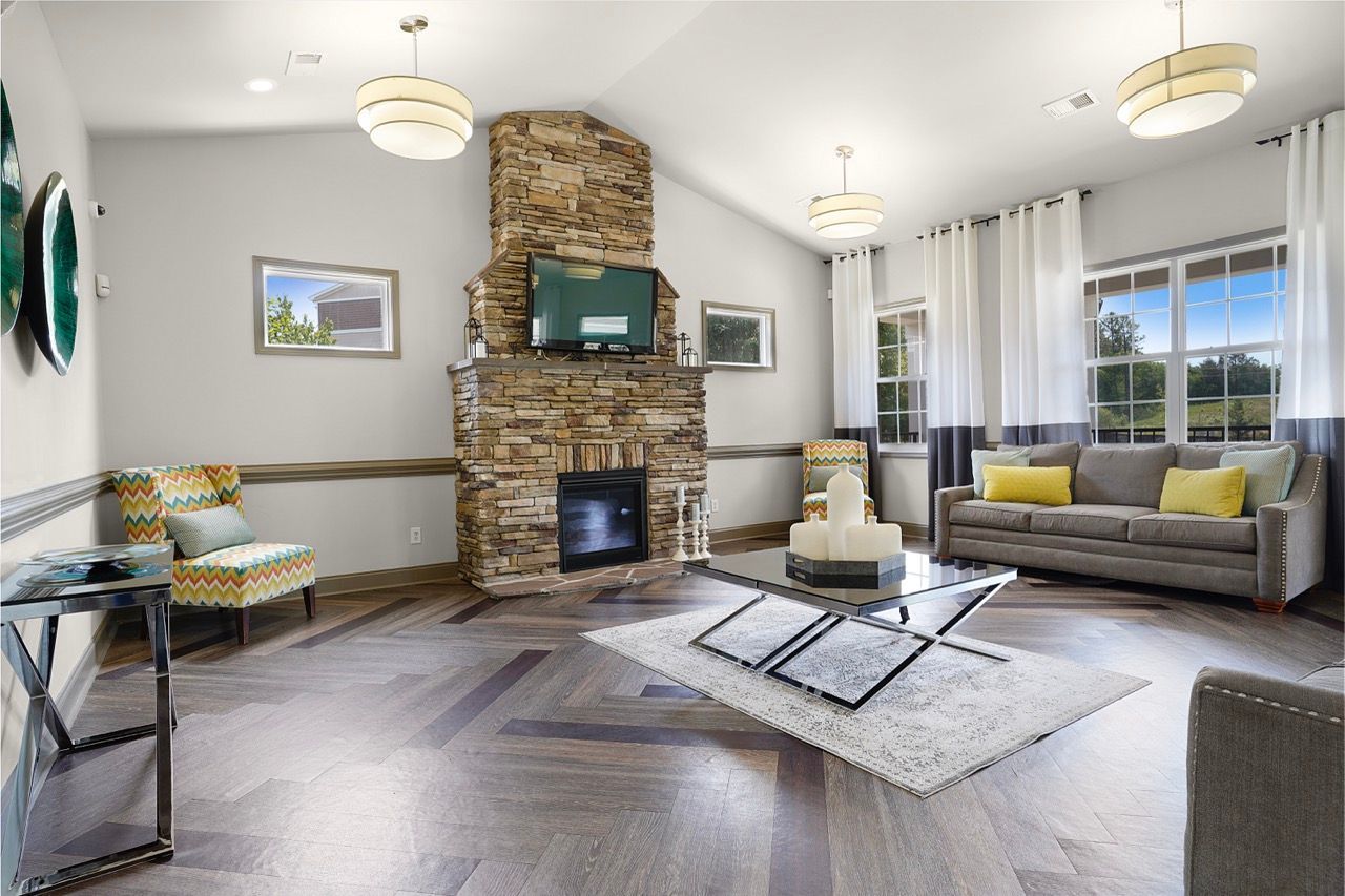 Living room with a stone fireplace, mounted TV, and large windows with white drapes at Reserve at Stone Hollow in Charlotte, NC.