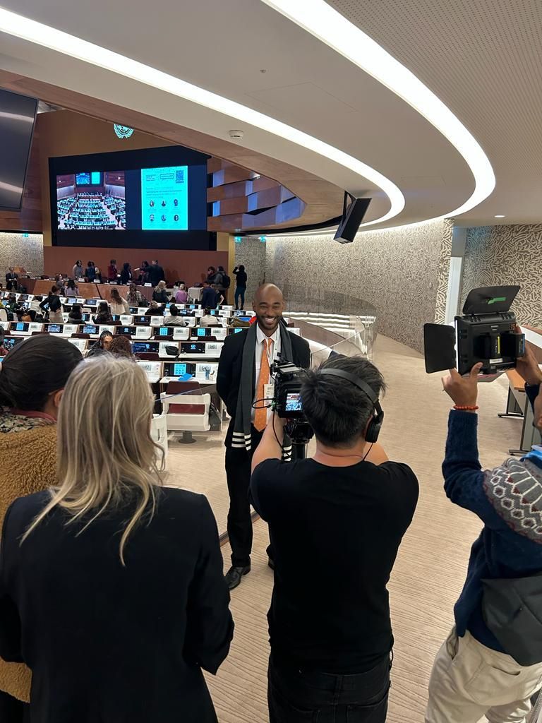 Sala de conferências com palestrante no pódio, plateia sentada e câmeras gravando a apresentação.