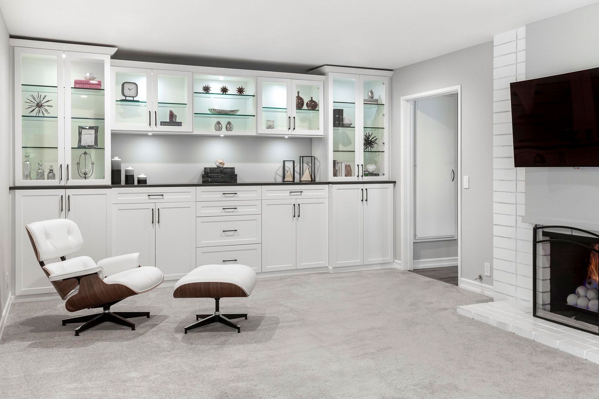 White built-in cabinetry with glass display shelves, a lounge chair, and a fireplace in a modern living room.