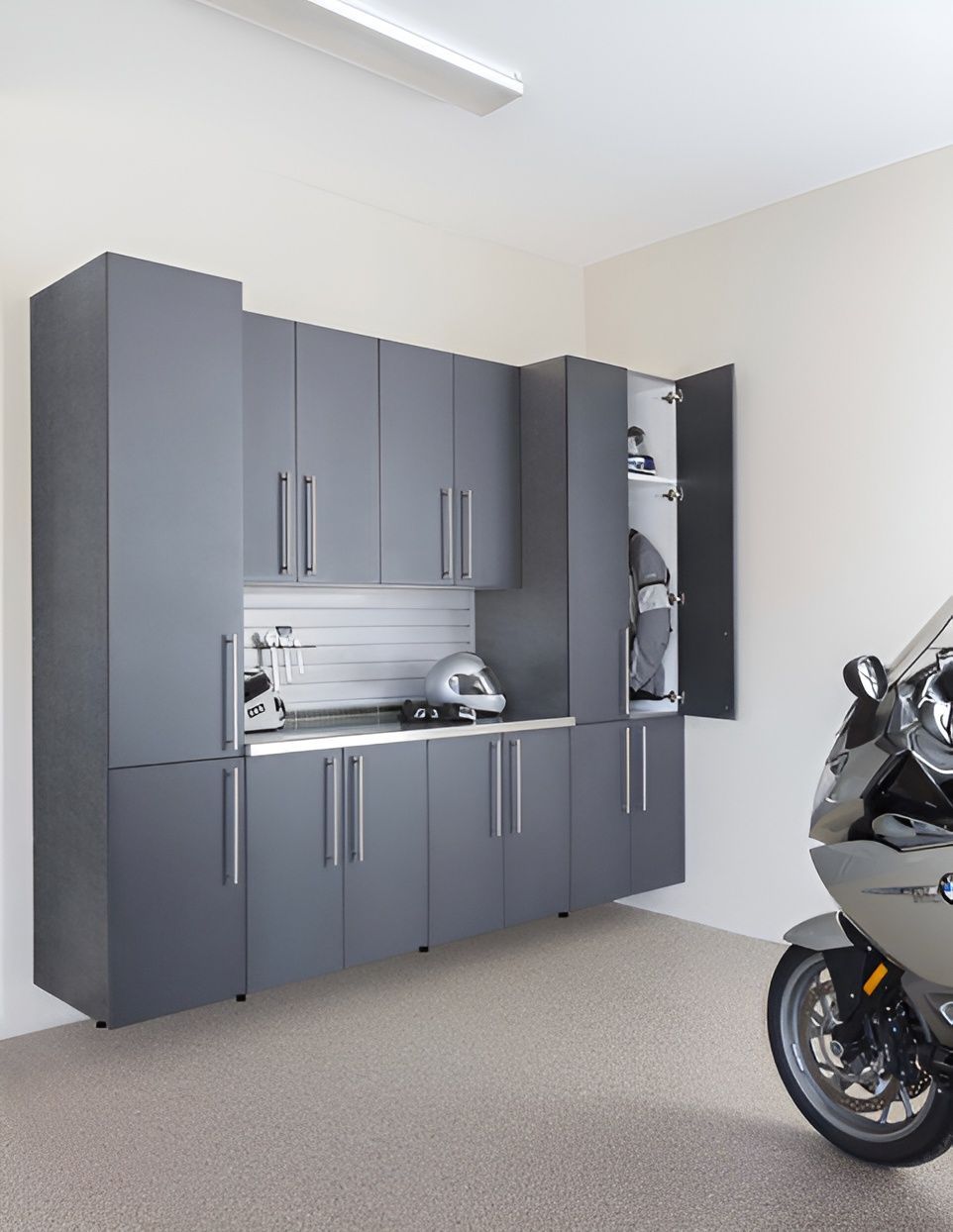 Modern garage cabinet workspace with wood cabinets, desk, wall-mounted TV, and black swivel chair