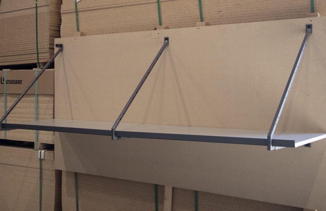 Shelf with metal brackets attached to a light brown wall, in front of a stack of plywood.