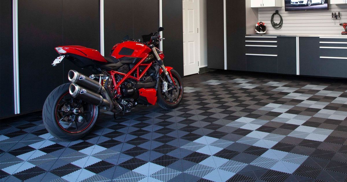 Red sport motorcycle parked on a checkered garage floor beside black cabinets and a workbench
