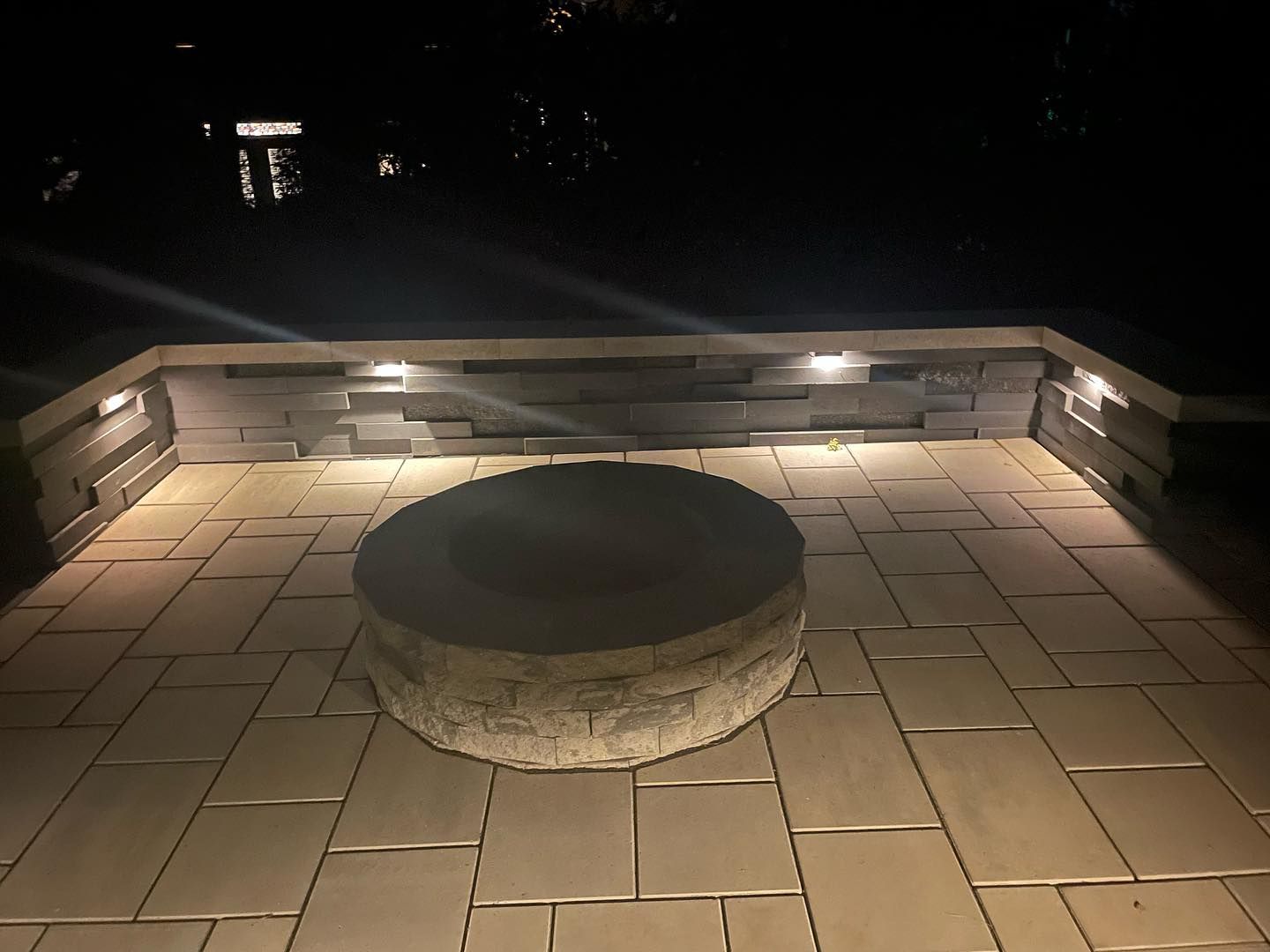 A fire pit is lit up at night on a patio.