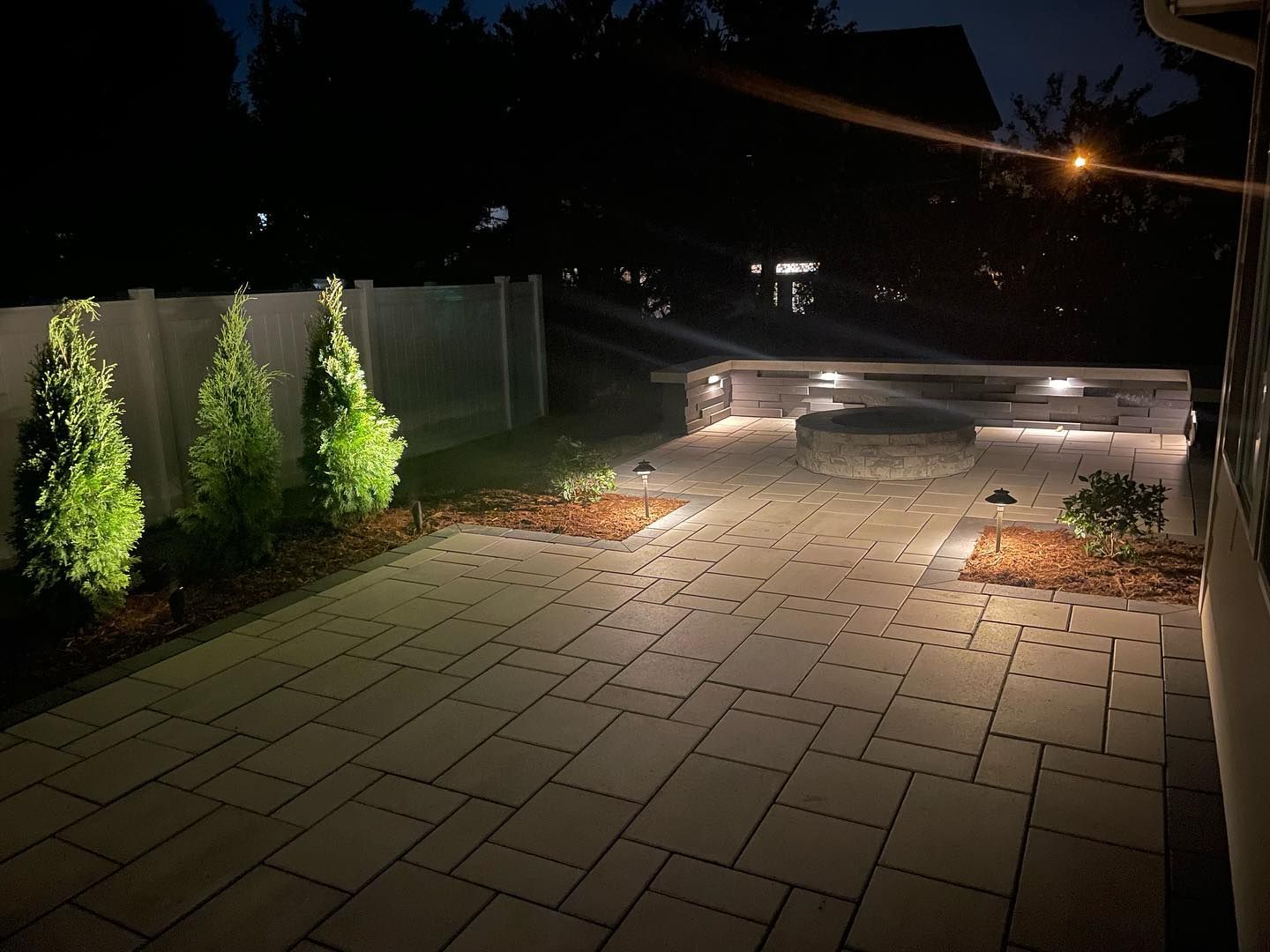 A patio with a fence and trees is lit up at night.